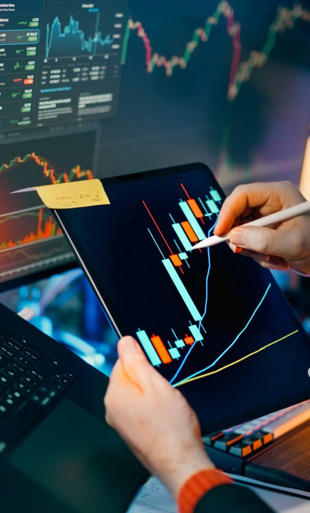 Trader analyzing stock market charts on tablet and monitor